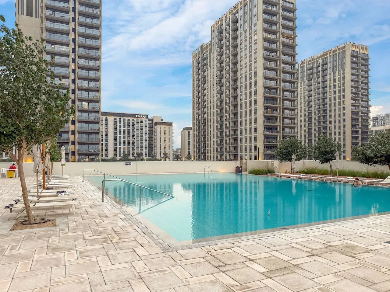 An outdoor swimming pool sits among paved seating areas and tall apartment buildings.