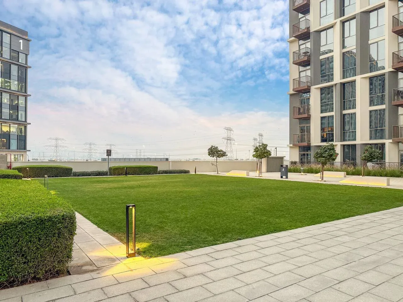 A landscaped courtyard with a broad lawn between modern apartment buildings.
