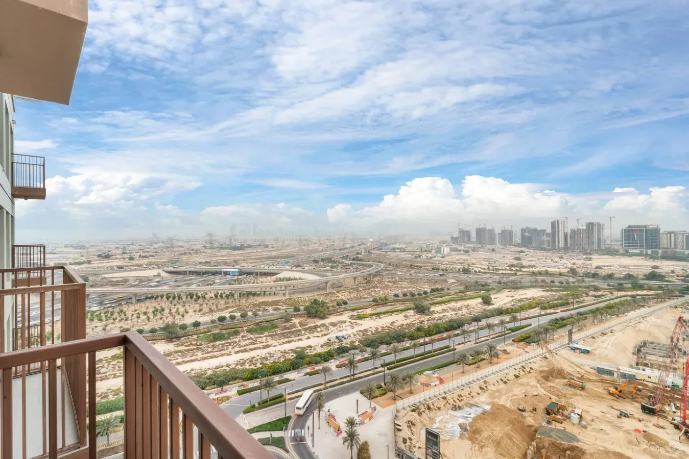 An elevated city view from a balcony, with roads and distant buildings beneath a cloudy sky.