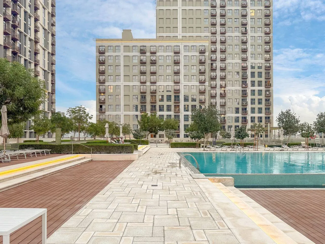 A paved walkway runs beside an outdoor swimming pool in a landscaped courtyard.