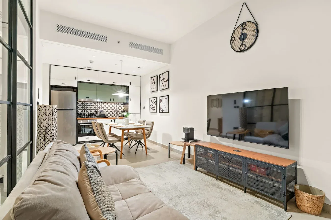 A bright living room with seating, a television, and a dining area in the background.