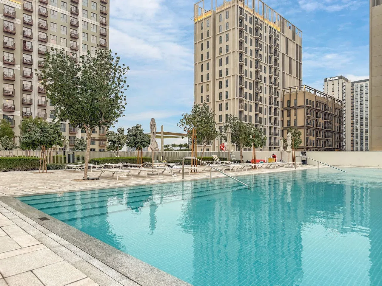 An outdoor swimming pool sits among tall residential buildings under a partly cloudy sky.