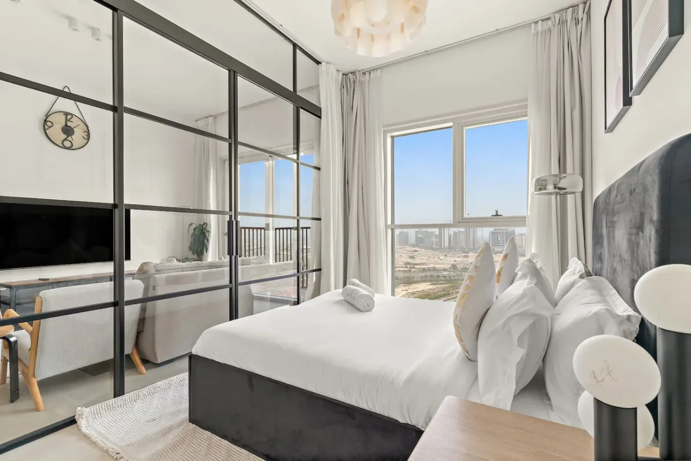 Un dormitorio luminoso con una cama tendida y grandes ventanas con vistas a la ciudad.