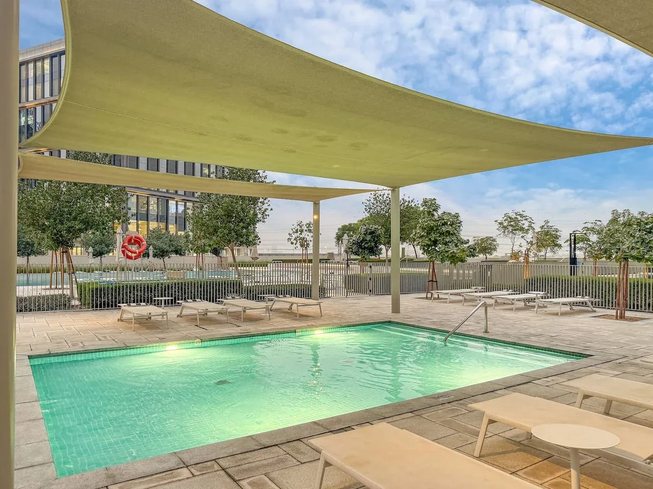 An outdoor swimming pool sits beneath a broad shade canopy, with loungers around it.