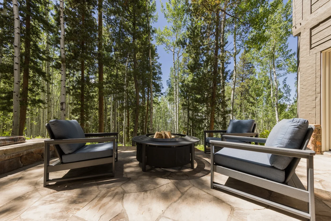 An outdoor deck seating area with a round fire pit surrounded by trees.