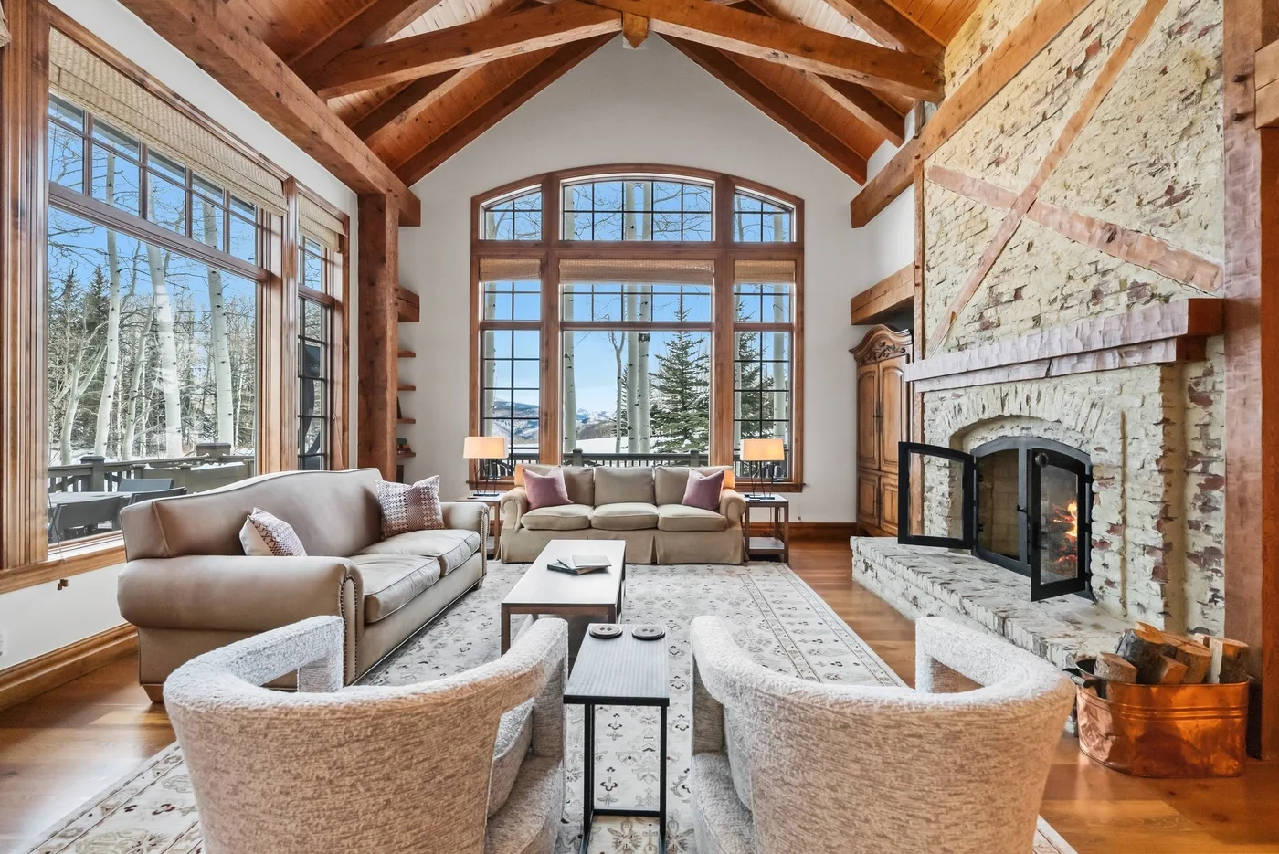 A spacious living room with tall windows, seating, and a large stone fireplace.
