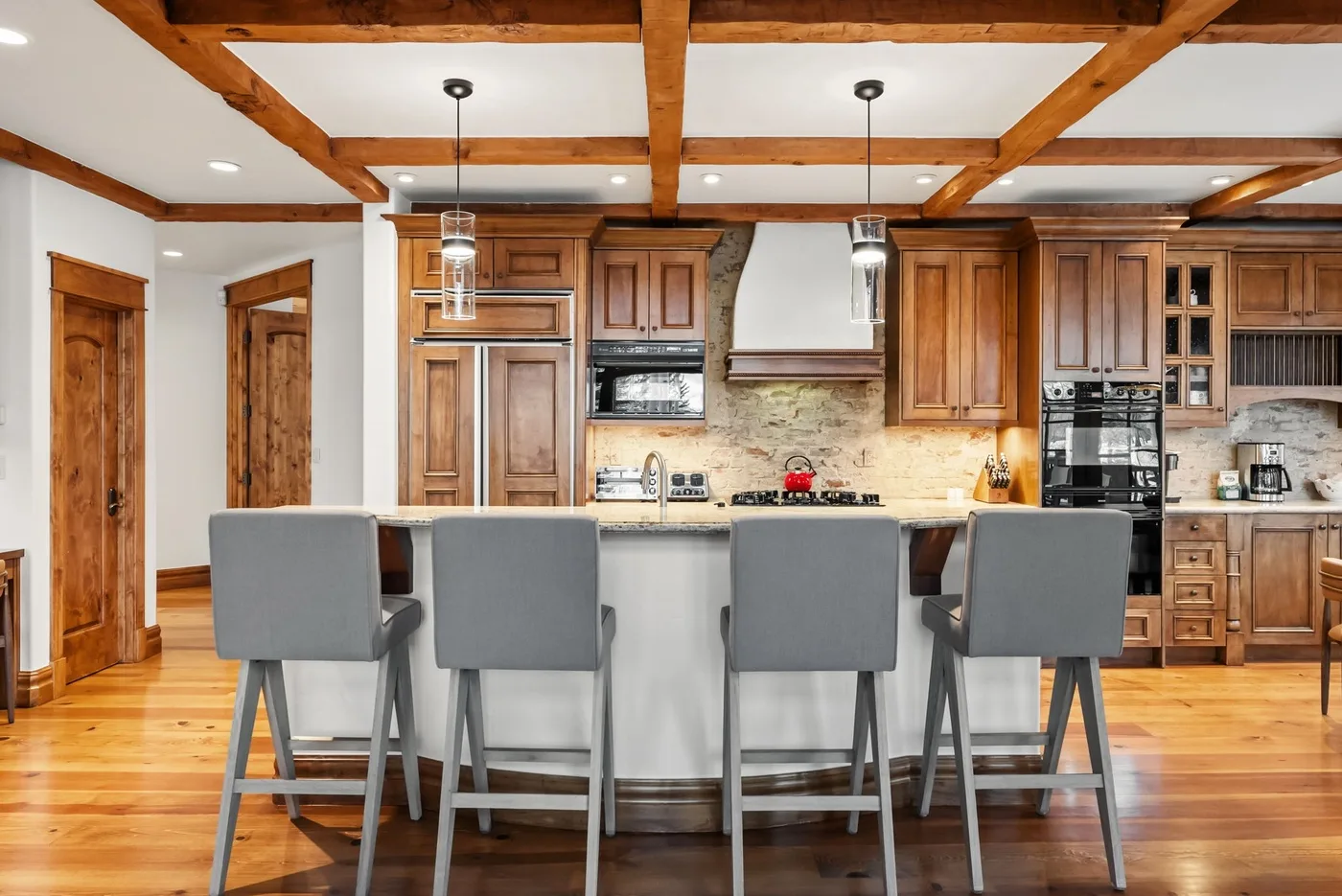 A wood-cabinet kitchen with a central island and seating beneath exposed ceiling beams.