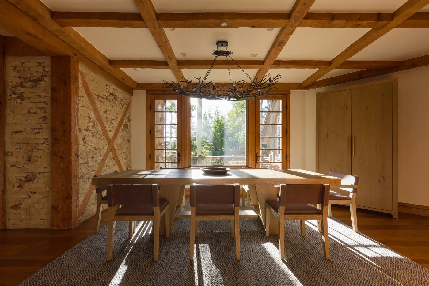 A dining room with a long wooden table beneath exposed ceiling beams.