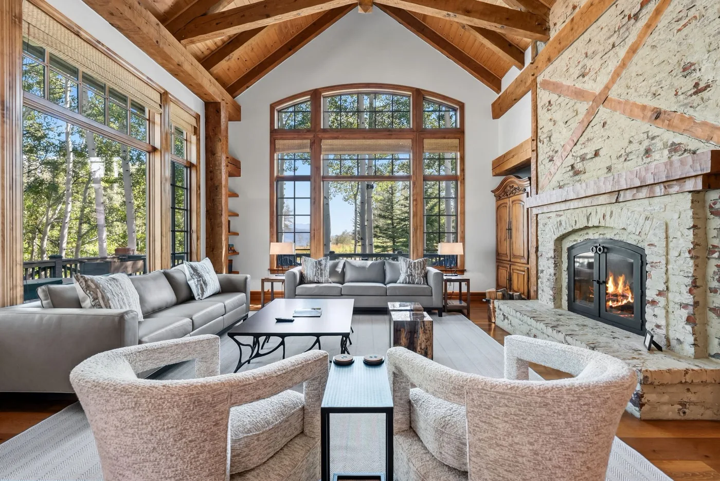 A spacious living room with large windows, exposed timber beams, and a fireplace.
