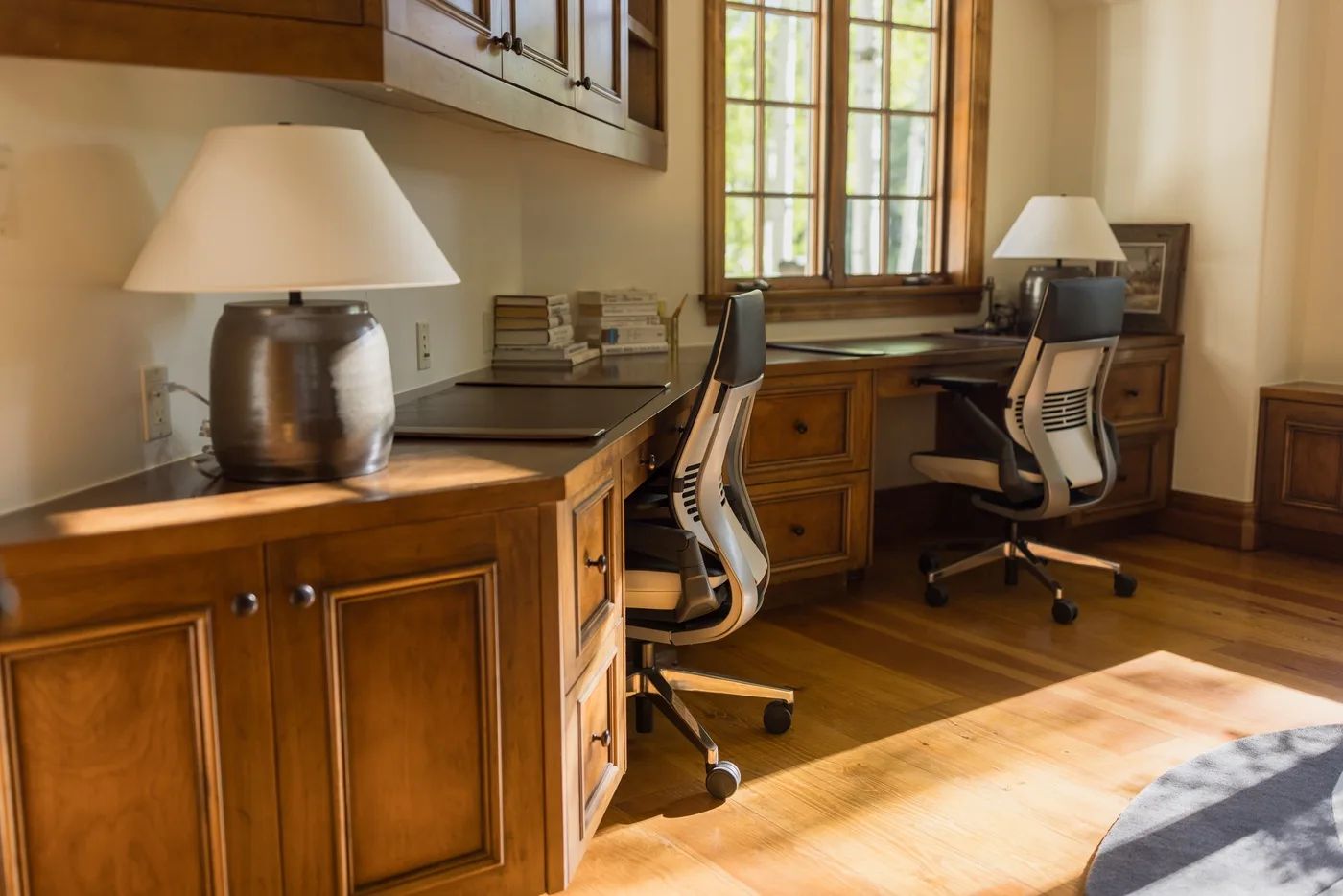 A home office with wooden desks, office chairs, and a sunlit window.
