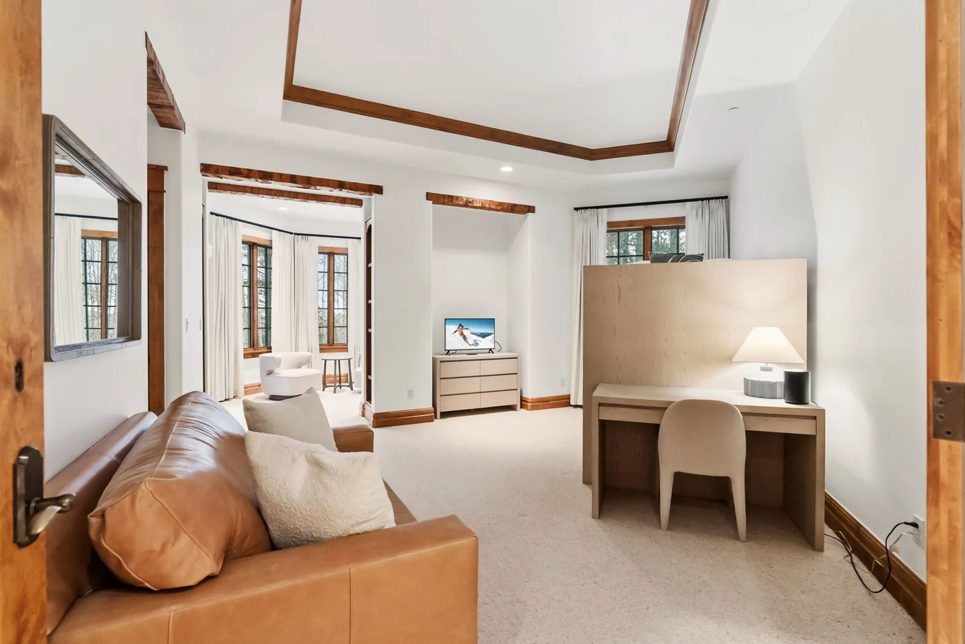 A bright bedroom seating area with a desk, lamp, and television.