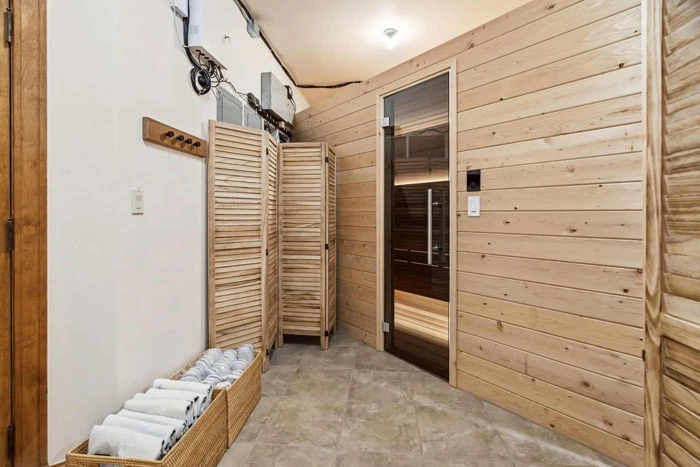 A wood-paneled sauna room with a dark glass door and folded towels.
