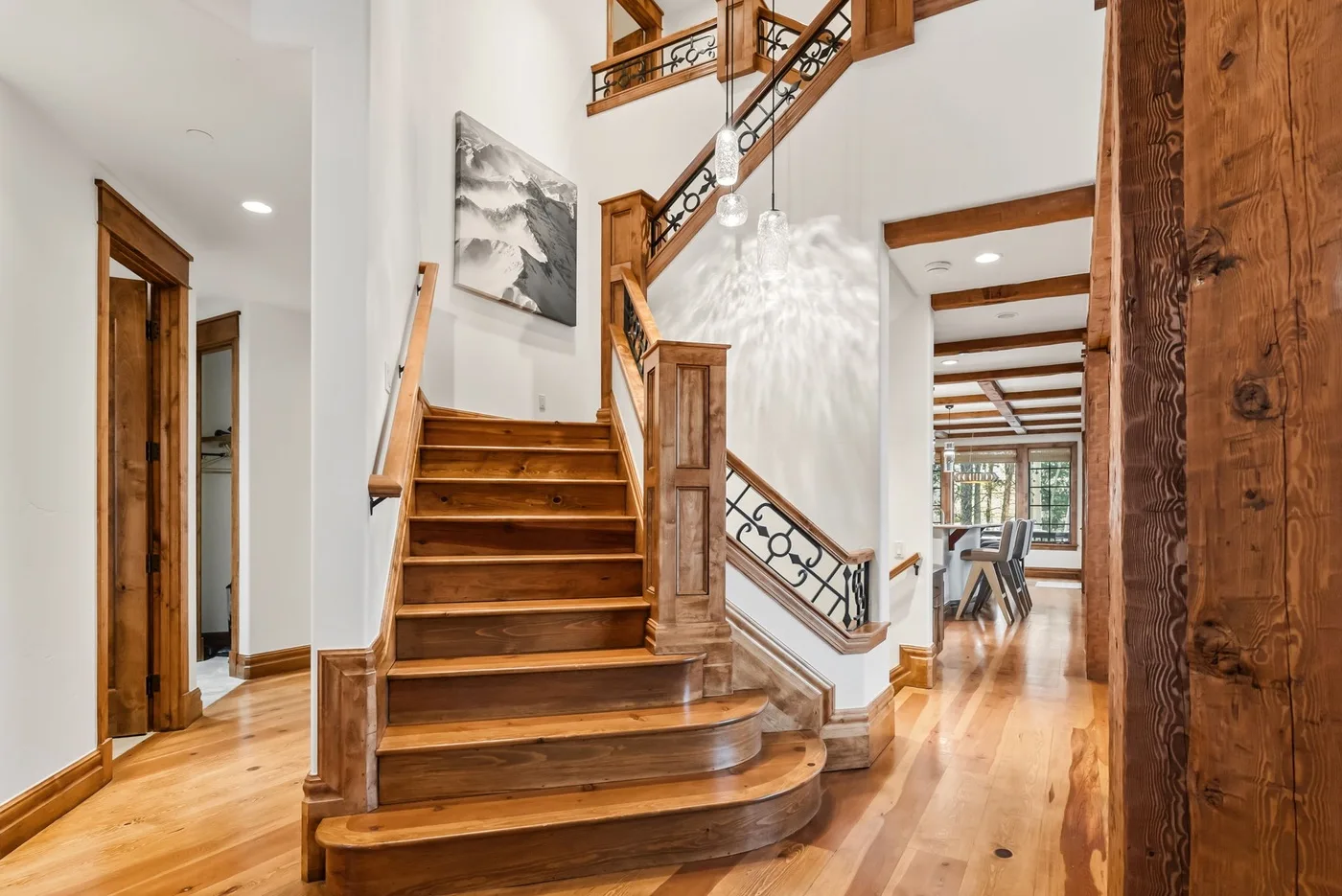 A wooden staircase and hallway with polished floors and a dining area beyond.