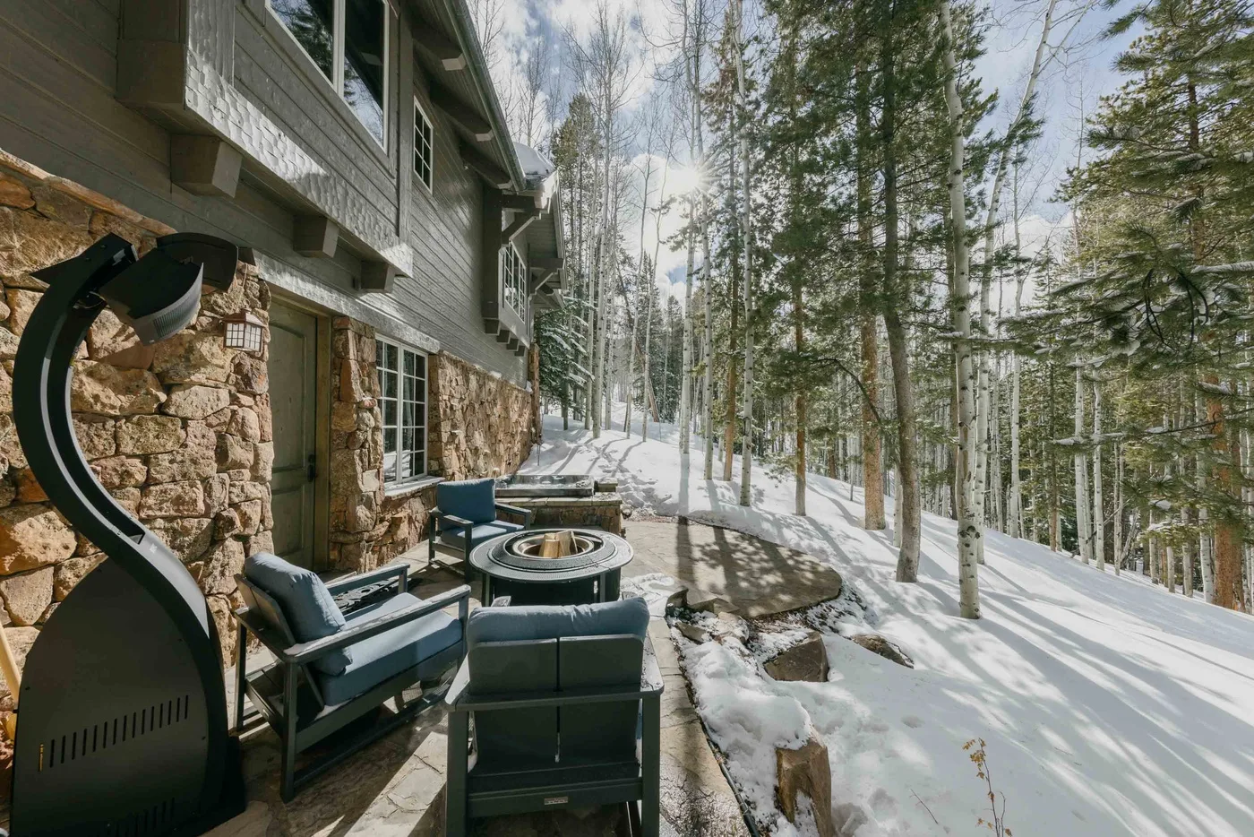 An outdoor seating area beside a stone-and-wood building overlooks a snowy forest.