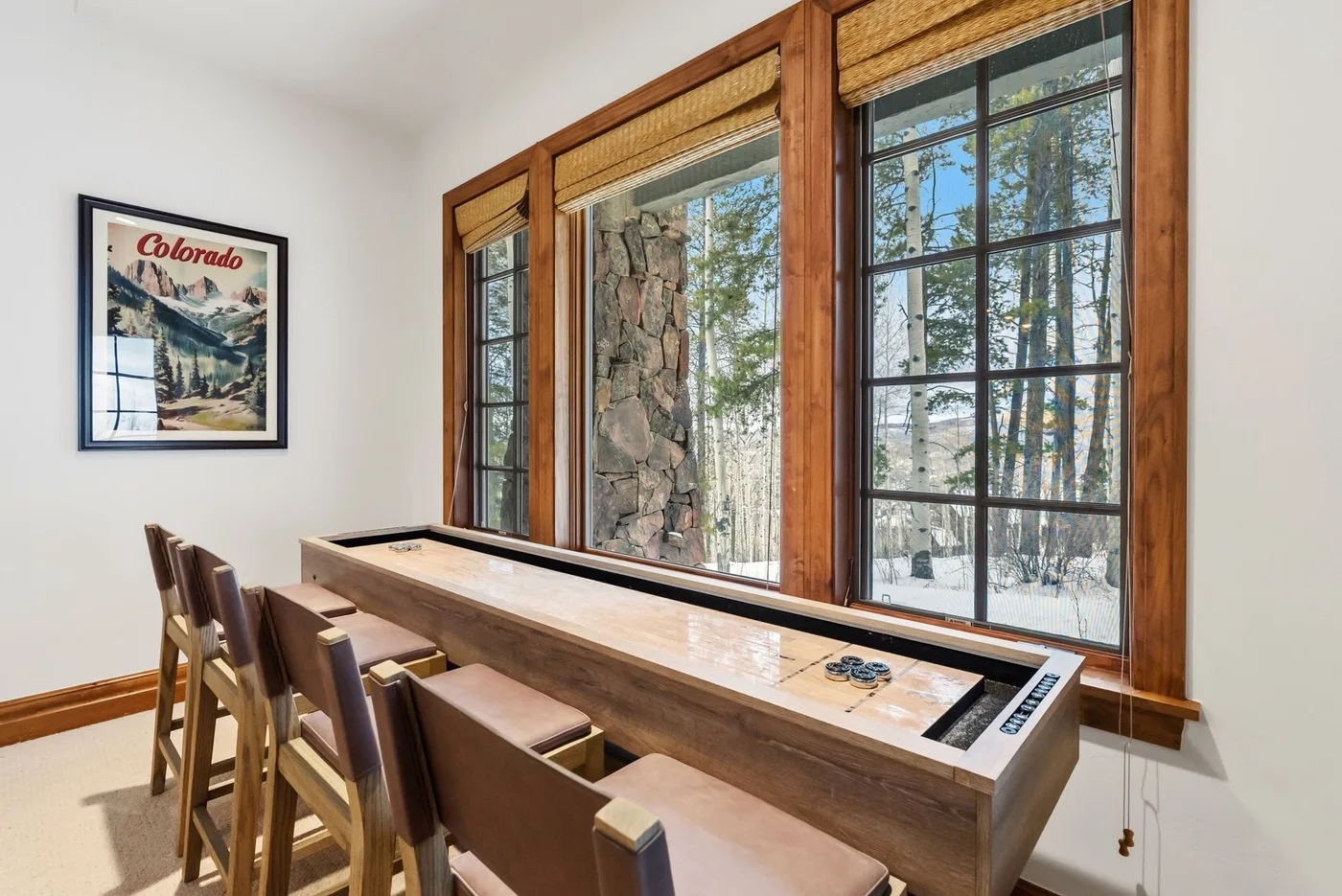 A bright game room with a shuffleboard table beside large windows.