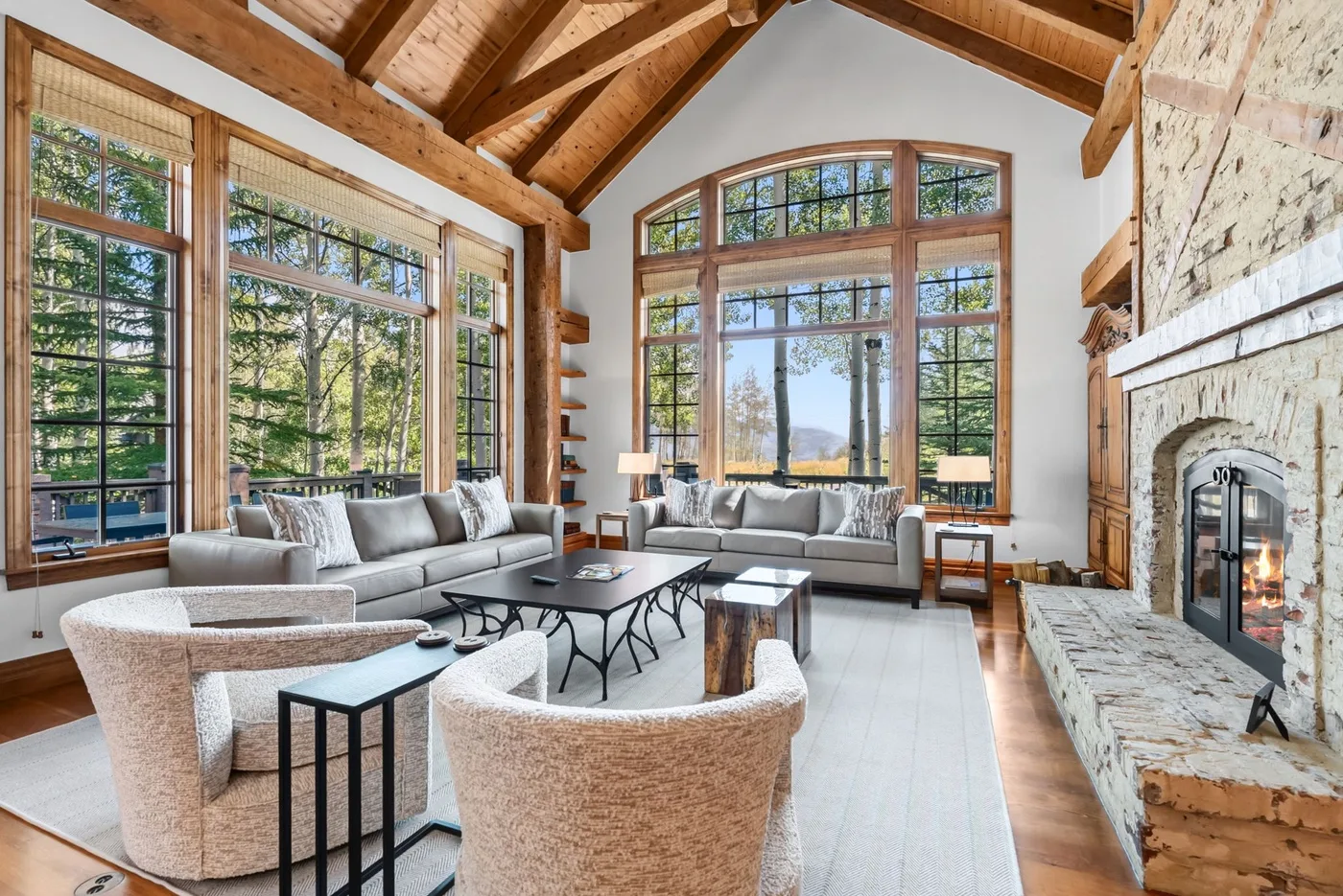 A spacious living room with large windows, seating, and a stone fireplace.