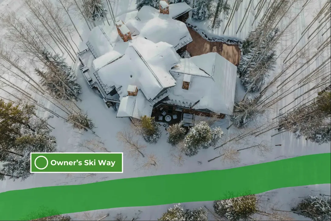 A snow-covered building sits among trees beside a broad green path.