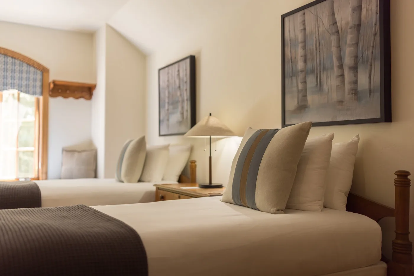 A bedroom with neatly made beds, neutral bedding, and framed artwork on the walls.