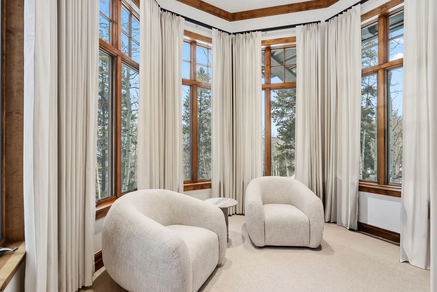 A bright sitting area with two upholstered seats beside tall windows.