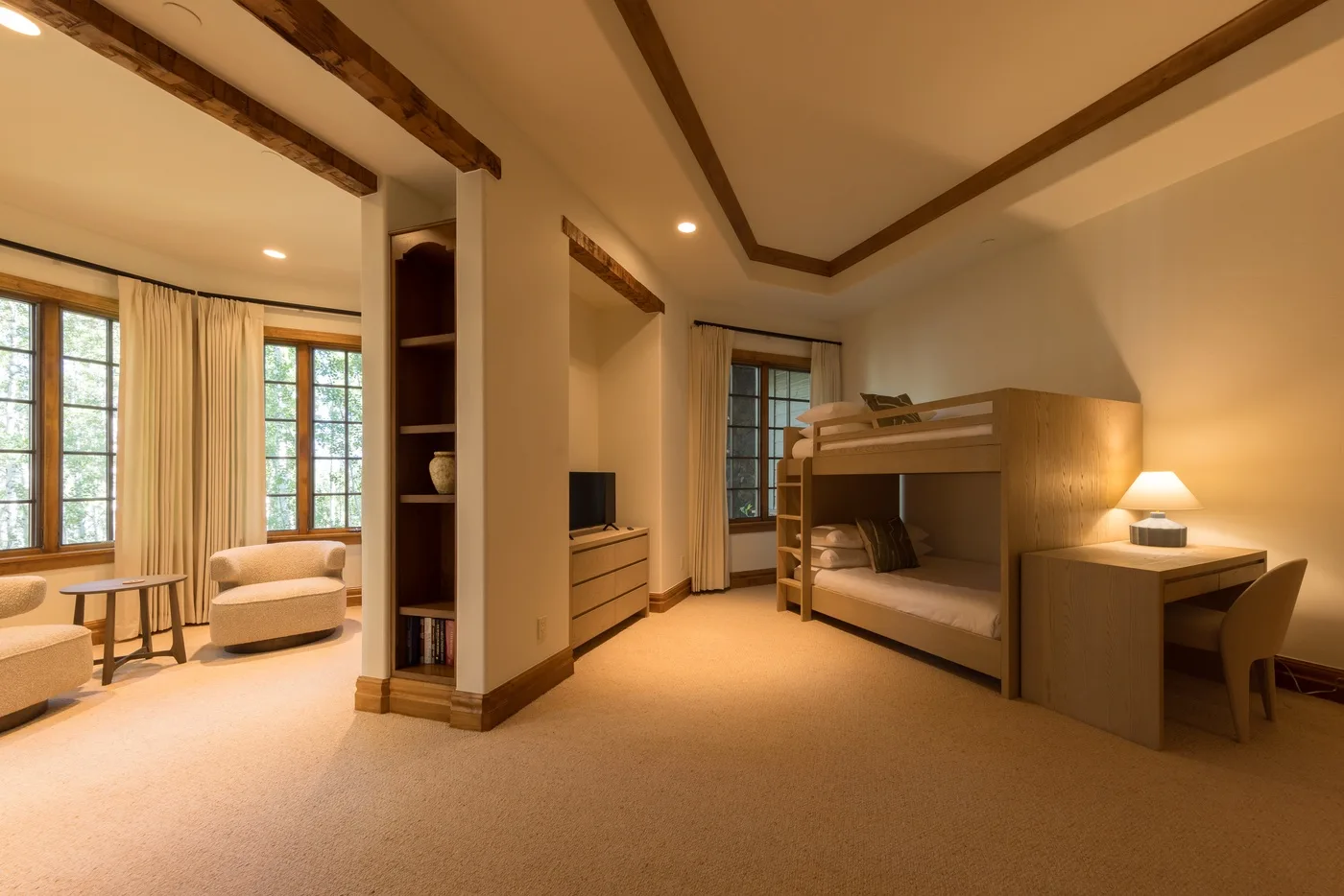 A warm bedroom with bunk beds, a desk, and a seating area by the windows.