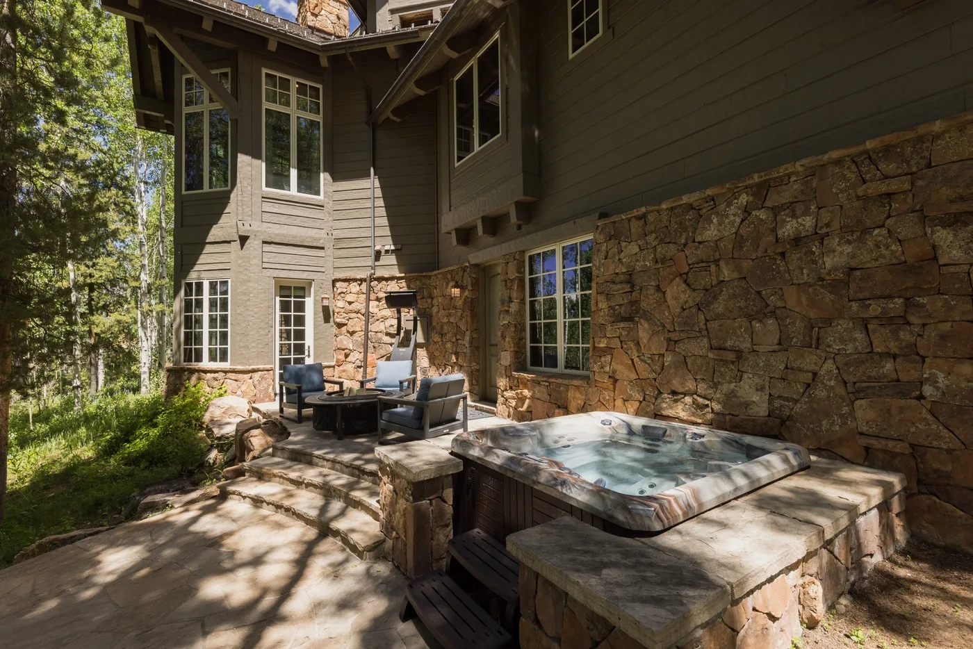 An outdoor patio with a hot tub beside a stone exterior wall.