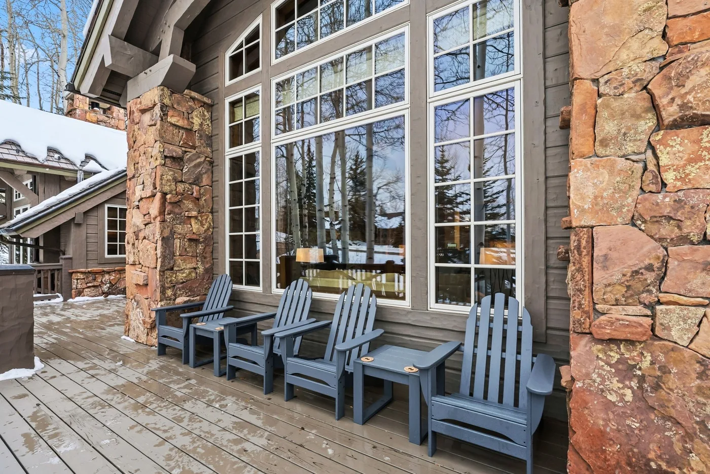 A wood deck with outdoor seating sits beside large windows and stone pillars.