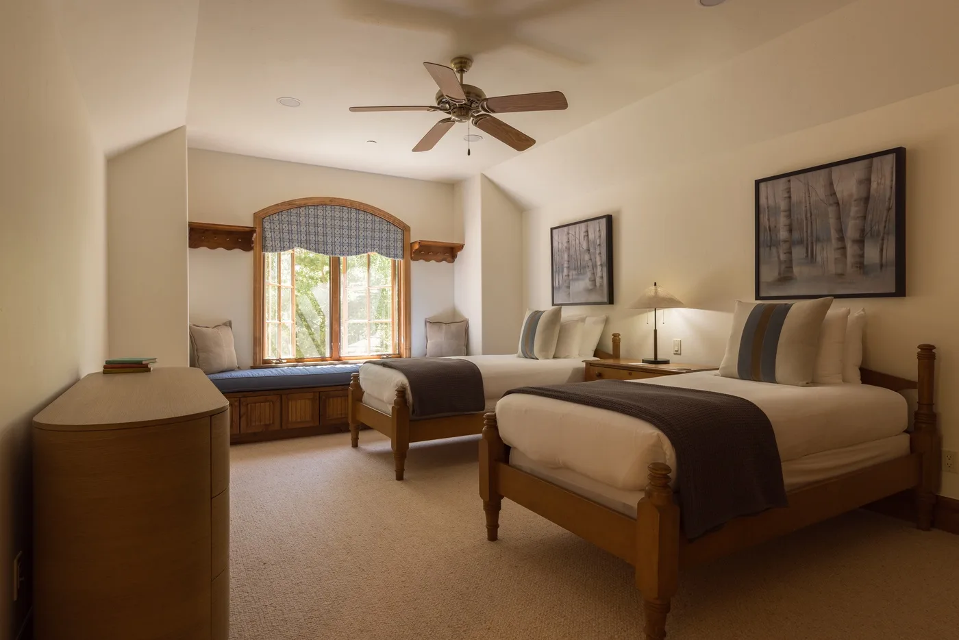 A bedroom with two beds, a ceiling fan, and a large window.