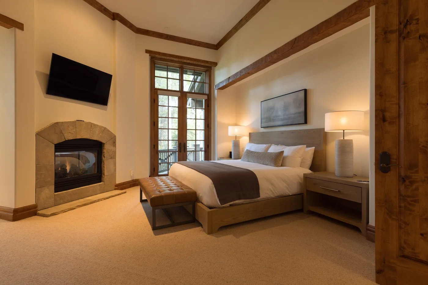 A bedroom with a neatly made bed and a stone fireplace.