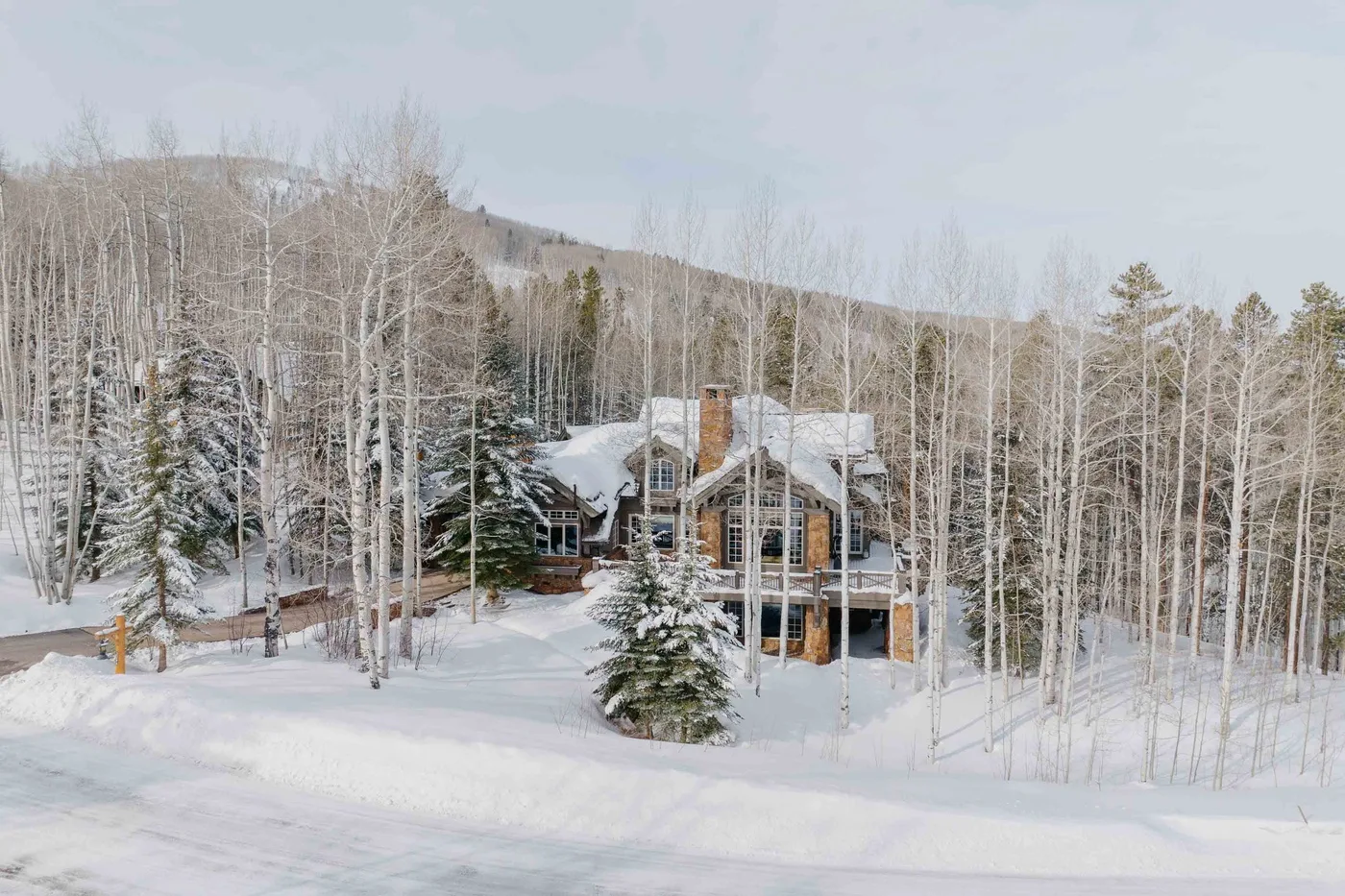A snow-covered house sits among leafless trees on a wooded hillside.