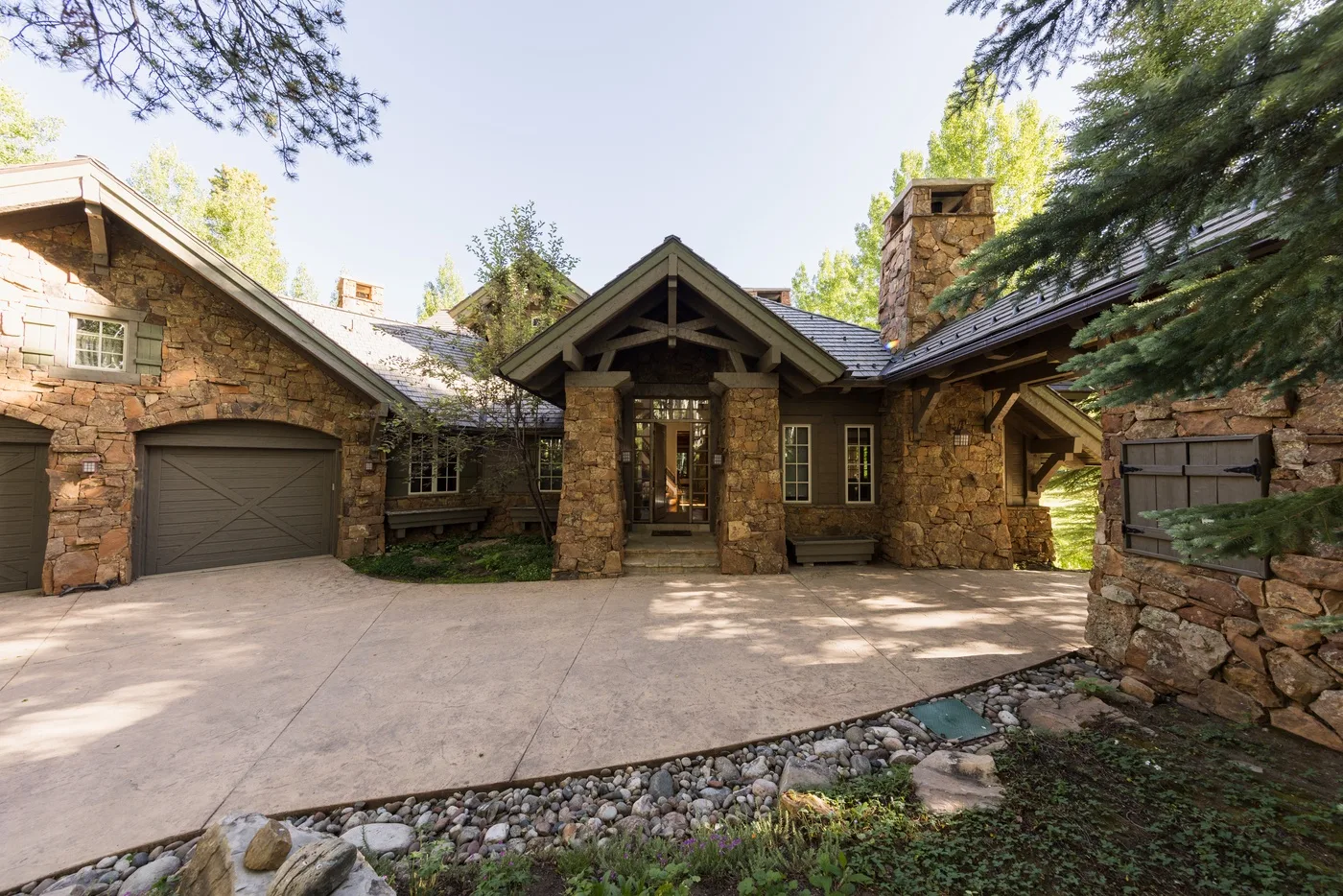 A stone house with a covered entrance and a wide paved driveway.