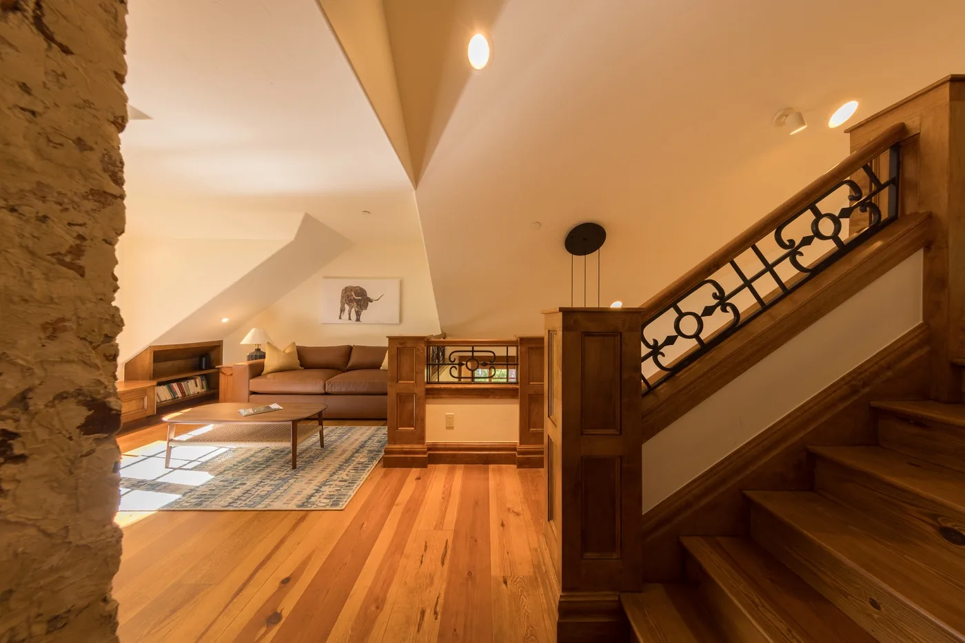 A warm living area sits beside a wooden staircase with decorative metal railing.