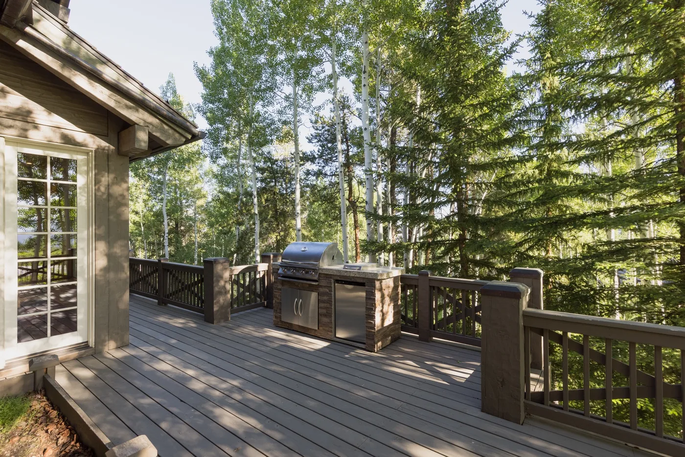 A wooden deck with an outdoor grill overlooks a wooded area.