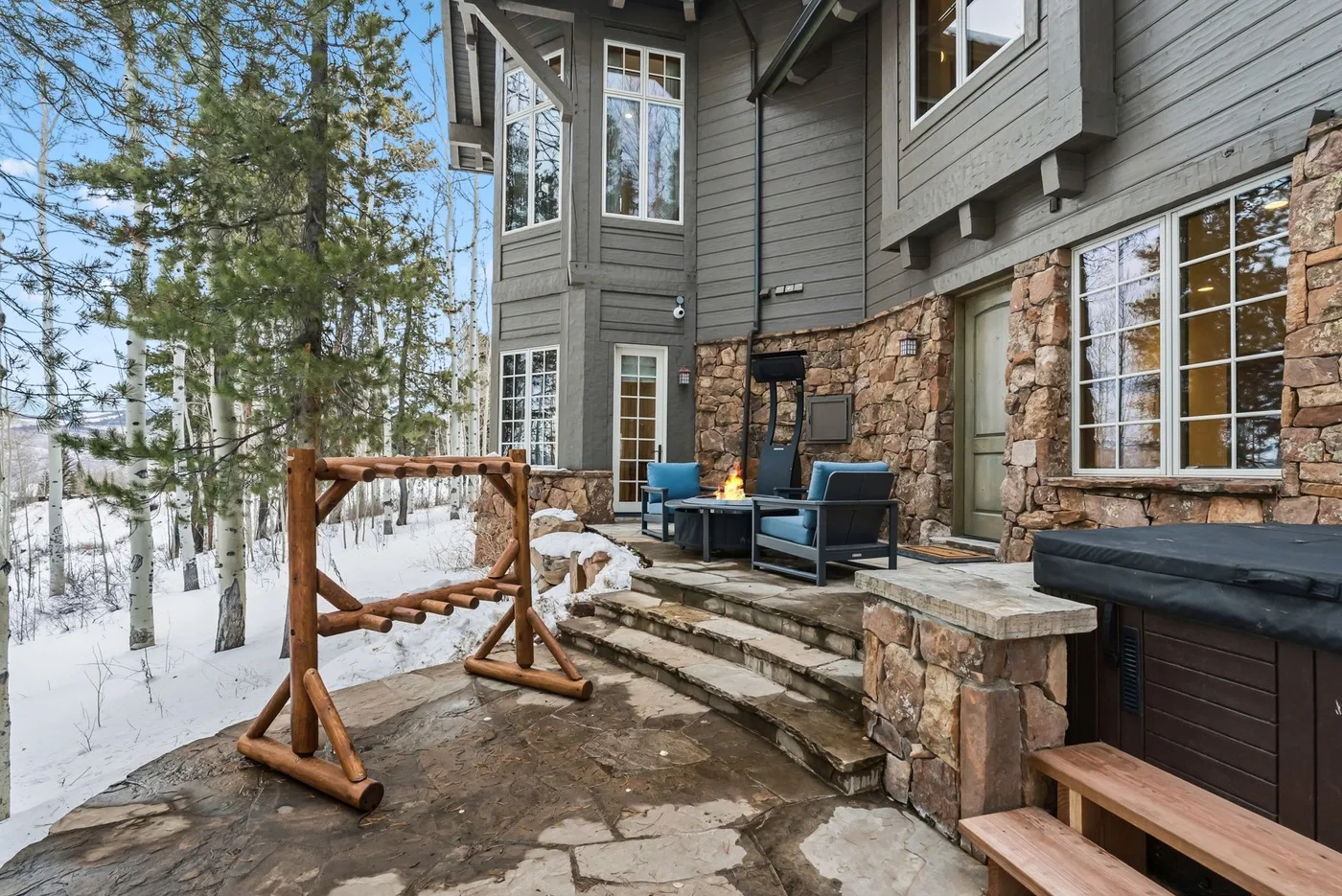 A stone patio beside a multi-story house, with outdoor seating and a small fire feature.