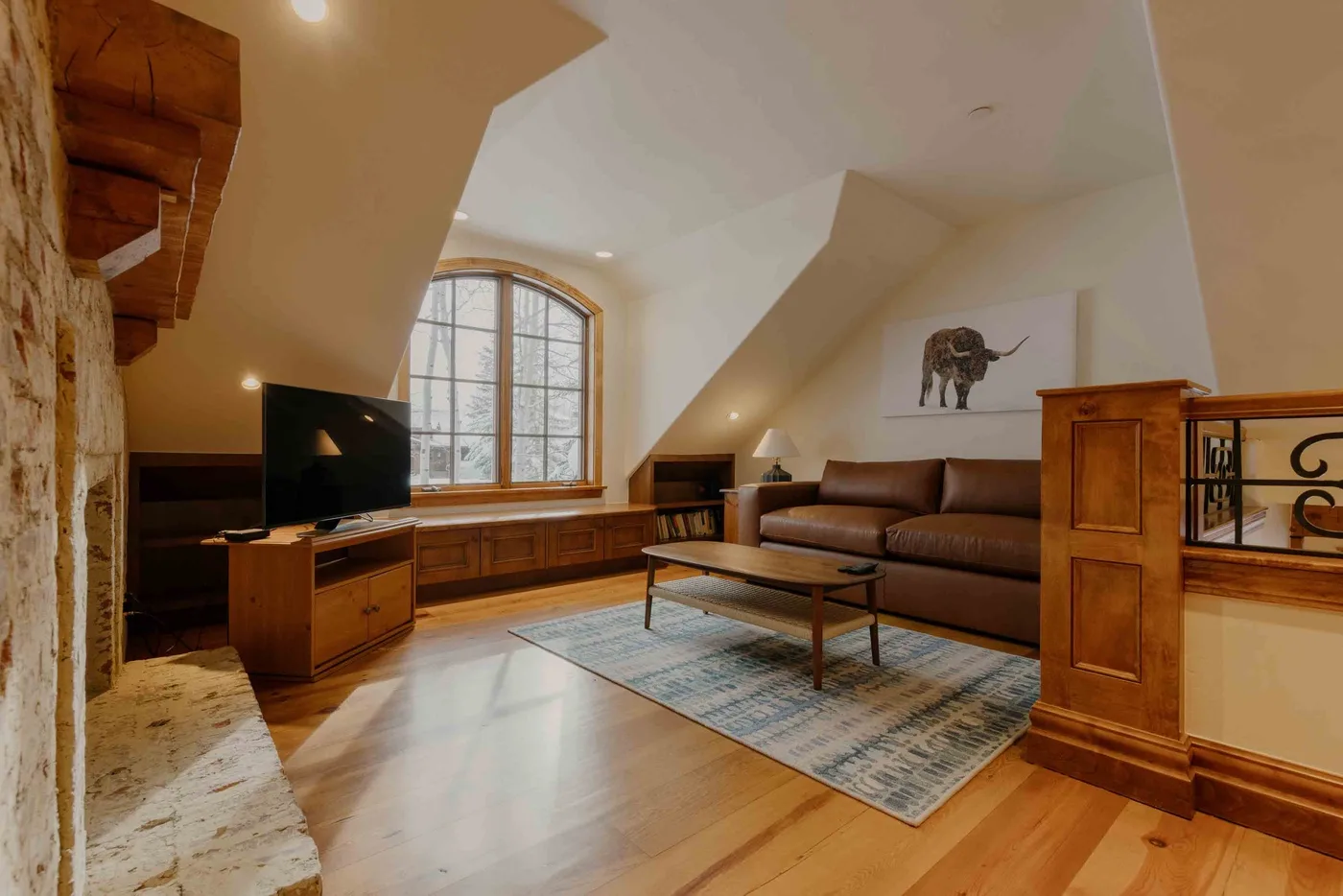 A living room with a brown seating area, a coffee table, and a large arched window.