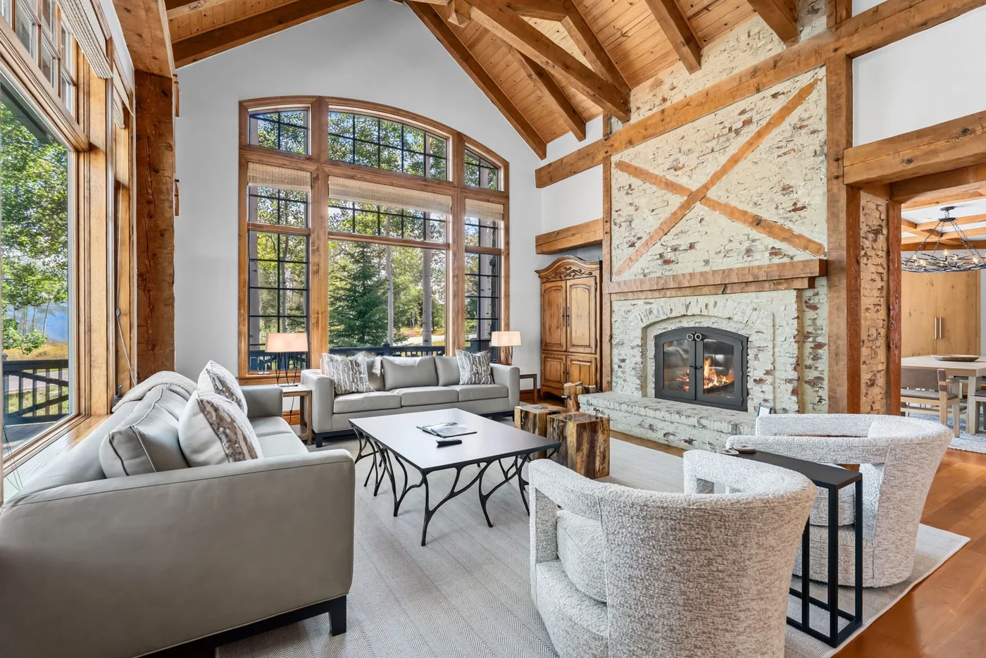 A spacious living room with large windows, seating, and a stone fireplace.