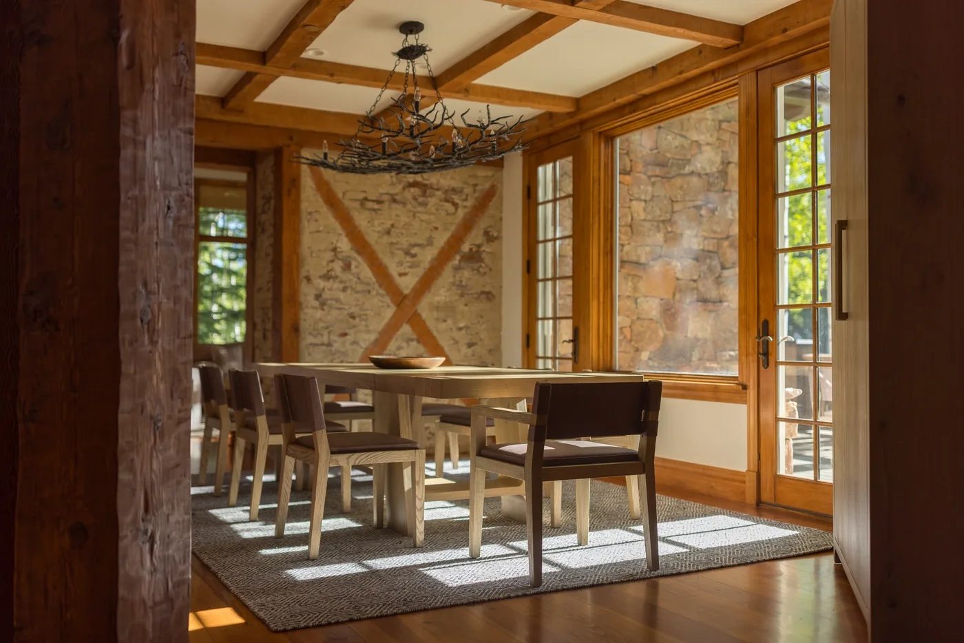 A dining room with a long wooden table and chairs beneath exposed ceiling beams.