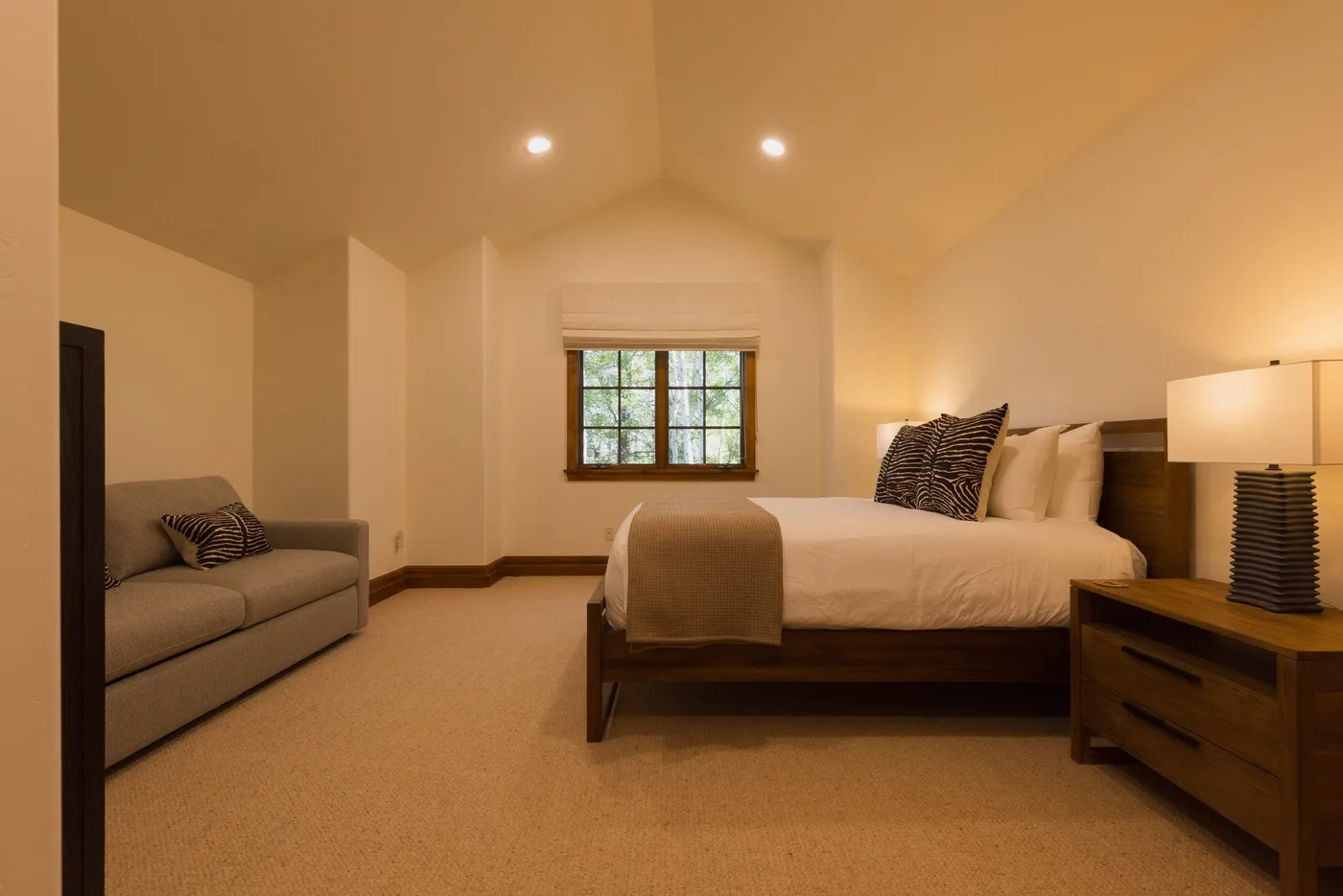 A bedroom with a bed, a small sofa, and a window.