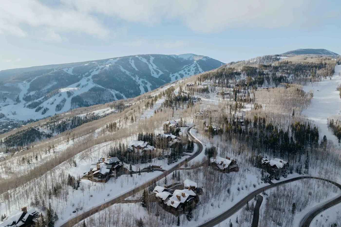 Aerial view of snow-covered mountain slopes, wooded hills, and winding roads.