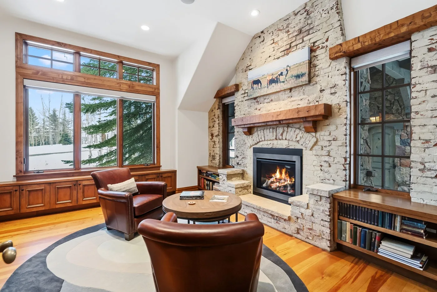 A living room with leather seating, large windows, and a stone fireplace.