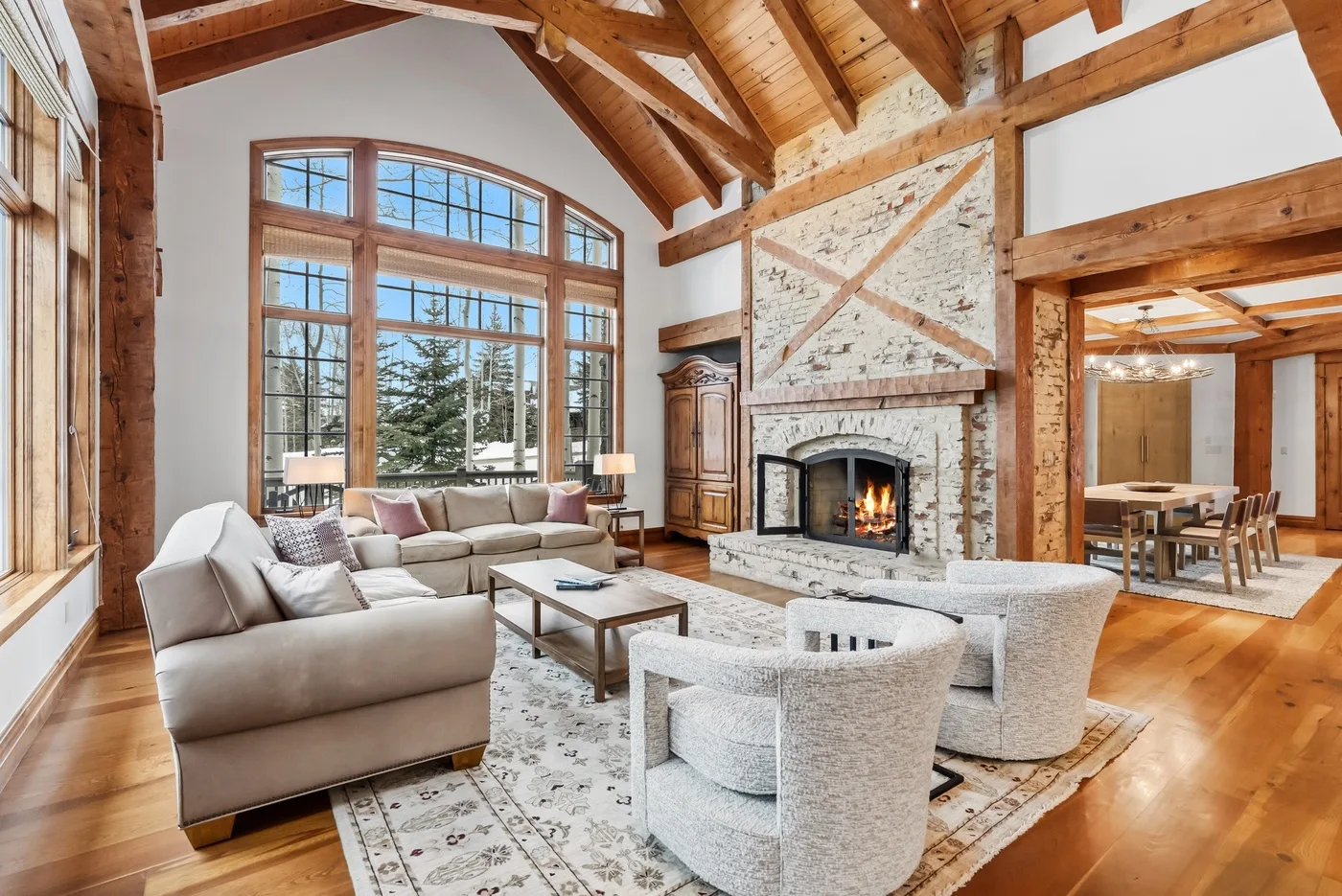 A spacious living room with exposed timber beams, large windows, and a stone fireplace.