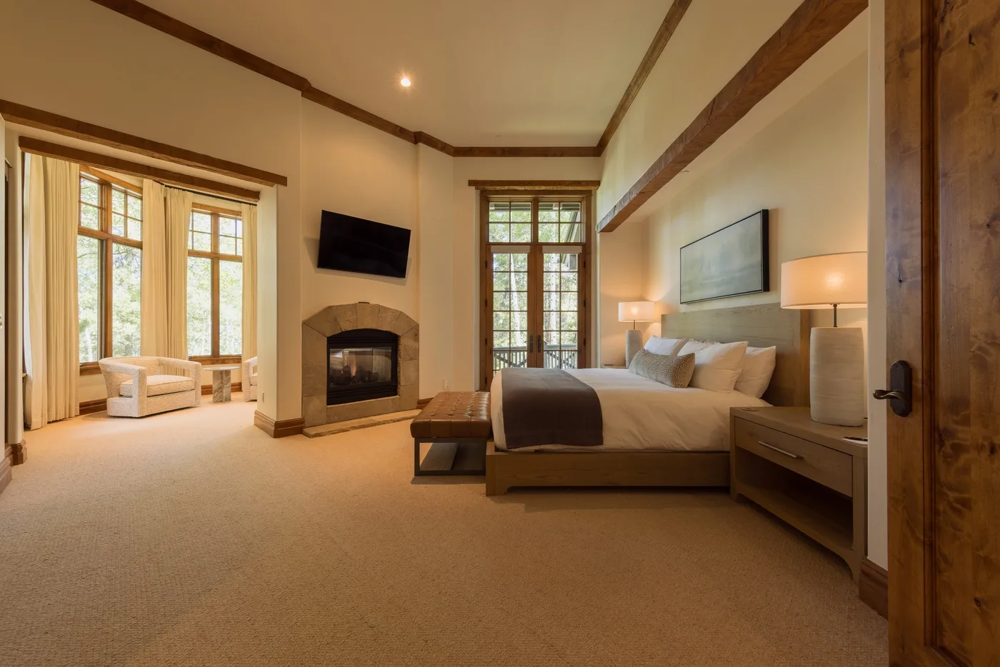 A bedroom with a bed, fireplace, and tall windows.