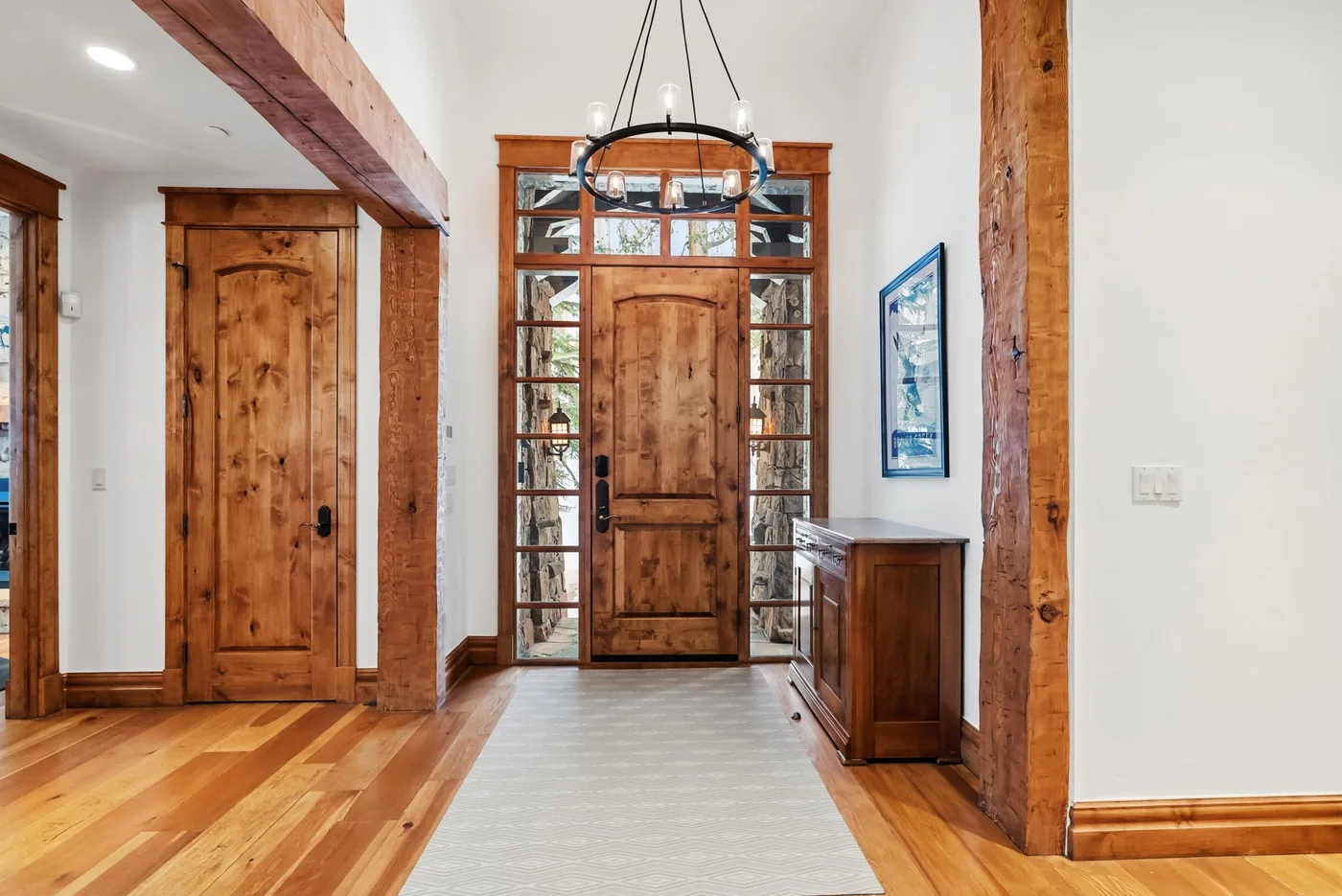 An entryway with a wooden front door, glass sidelights, and a runner rug.
