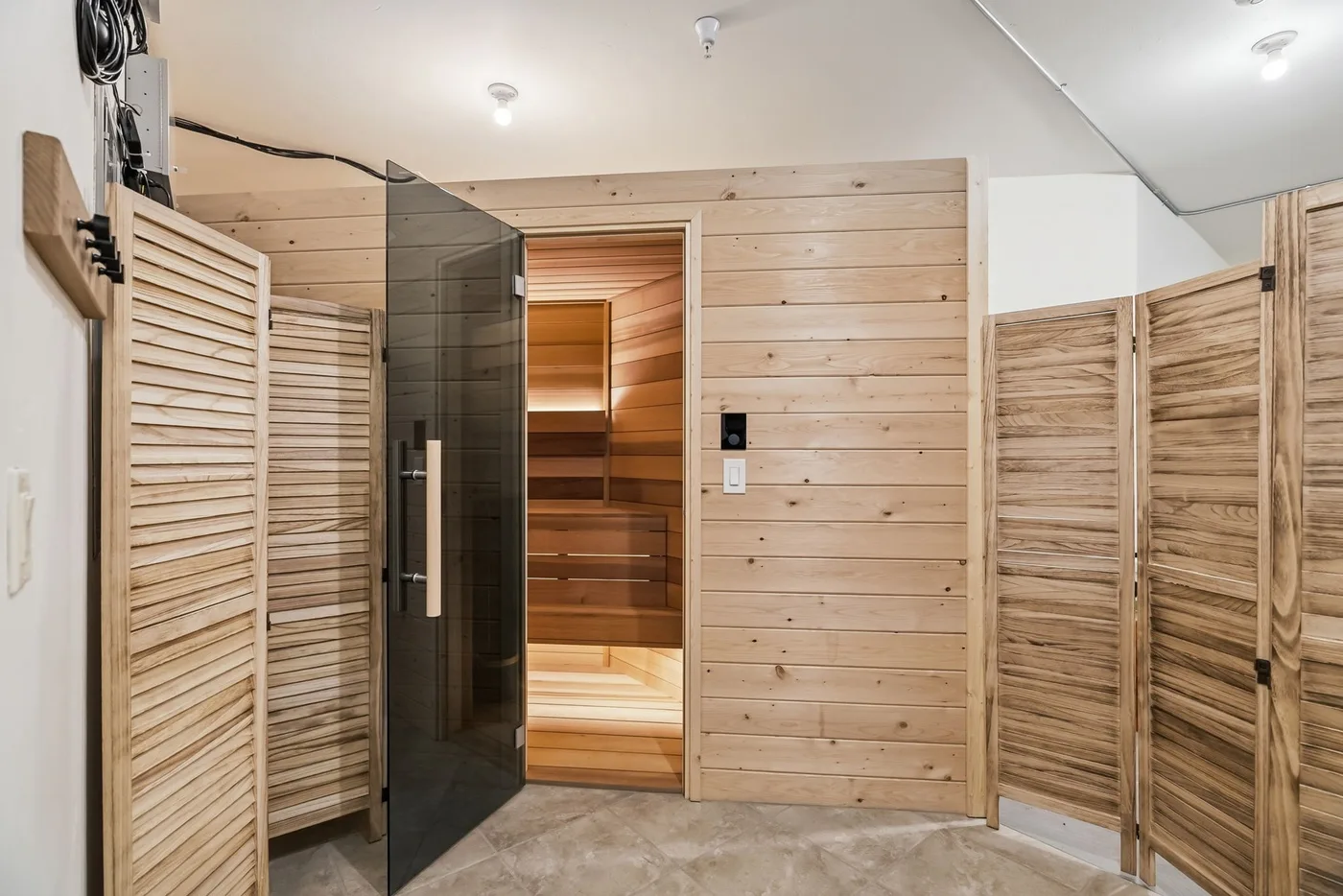 A wood-paneled sauna room with a dark glass door and wooden partitions.