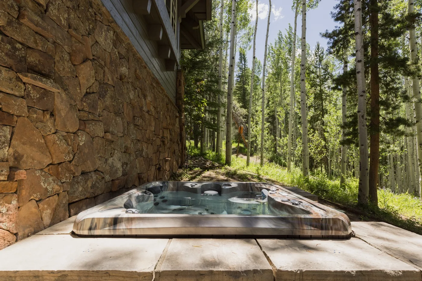 An outdoor hot tub sits on a stone patio beside a wooded cabin.