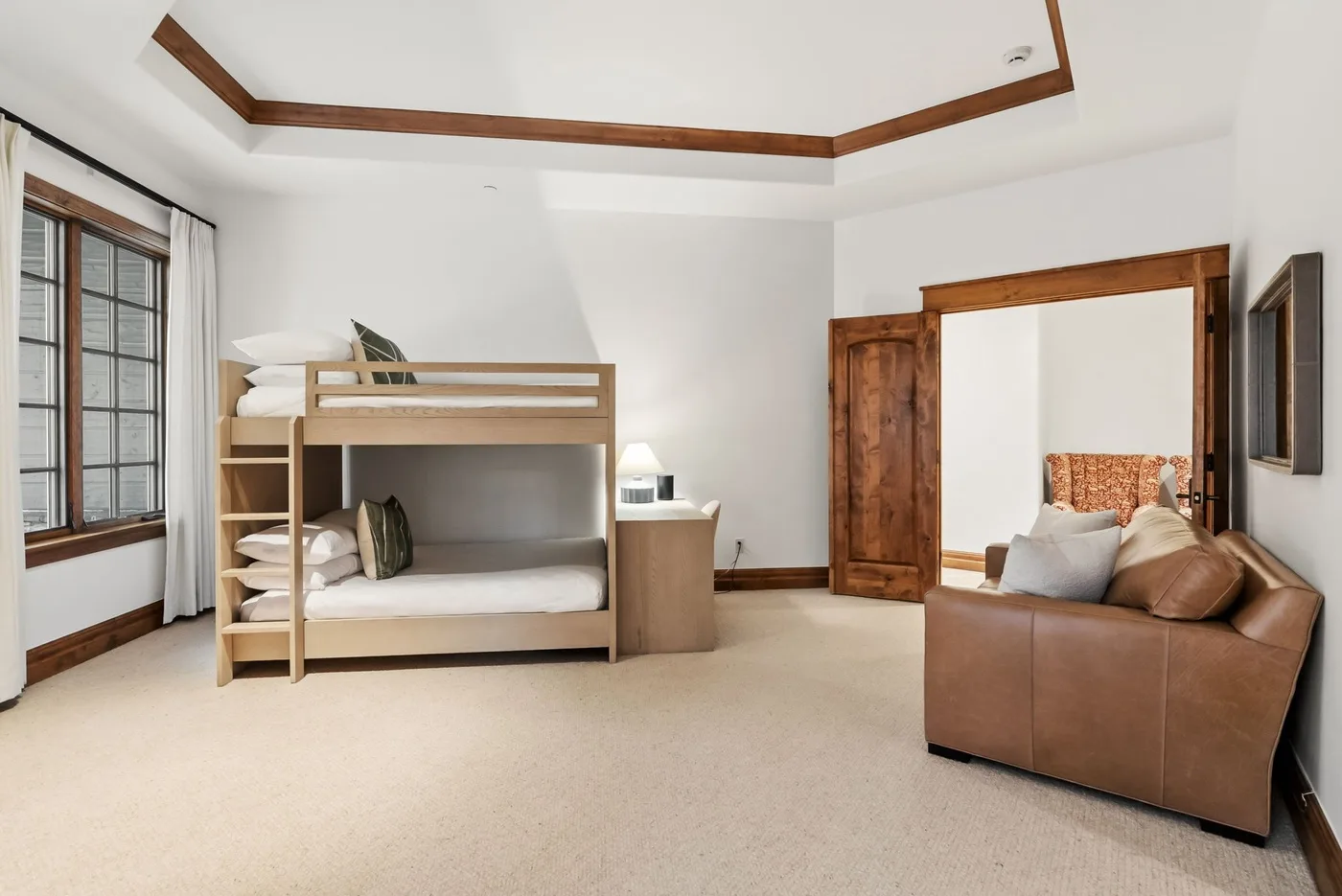 A bright bedroom with a wooden bunk bed and a brown sofa.
