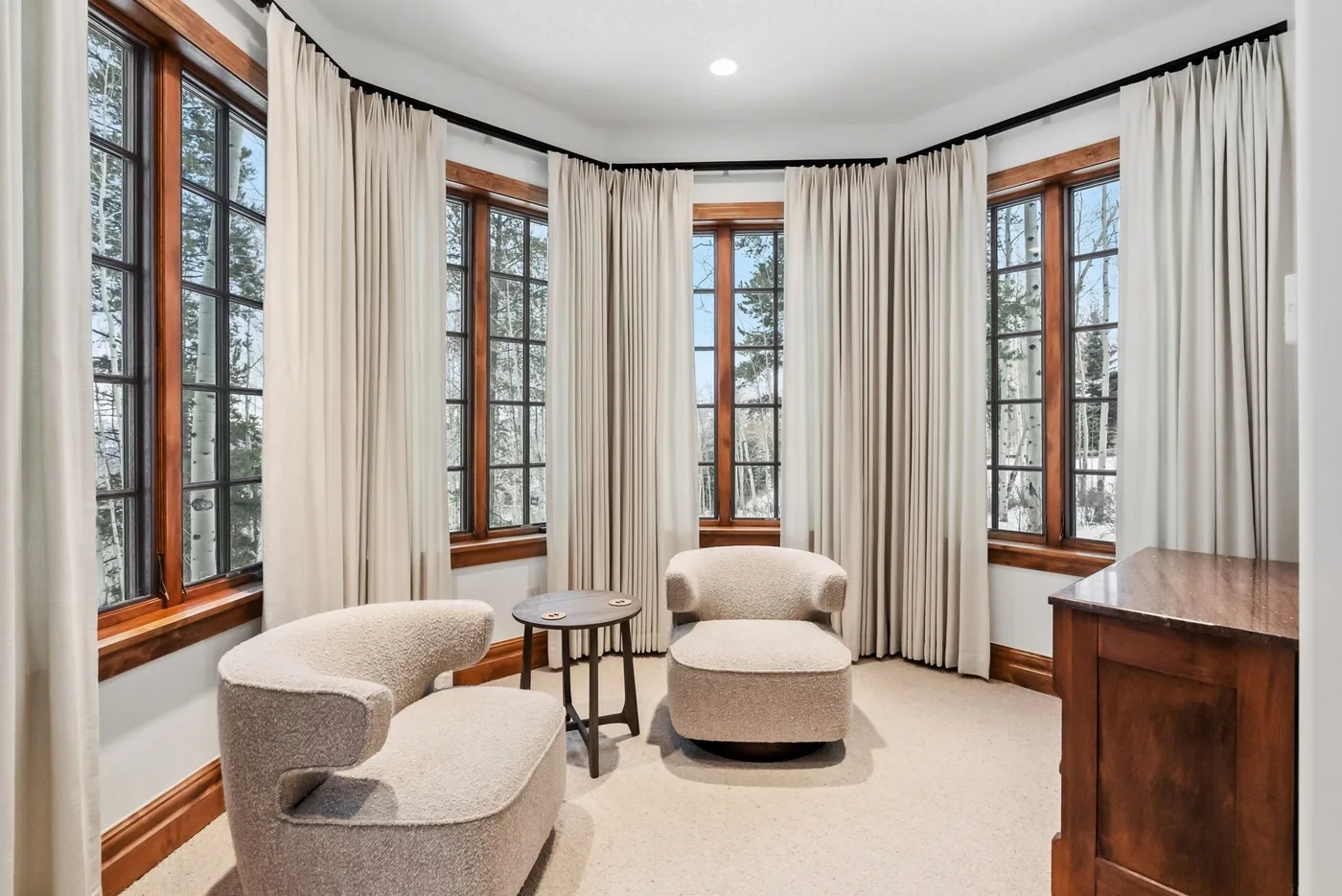 A bright sitting room with curved bay windows, light curtains, and upholstered seating.