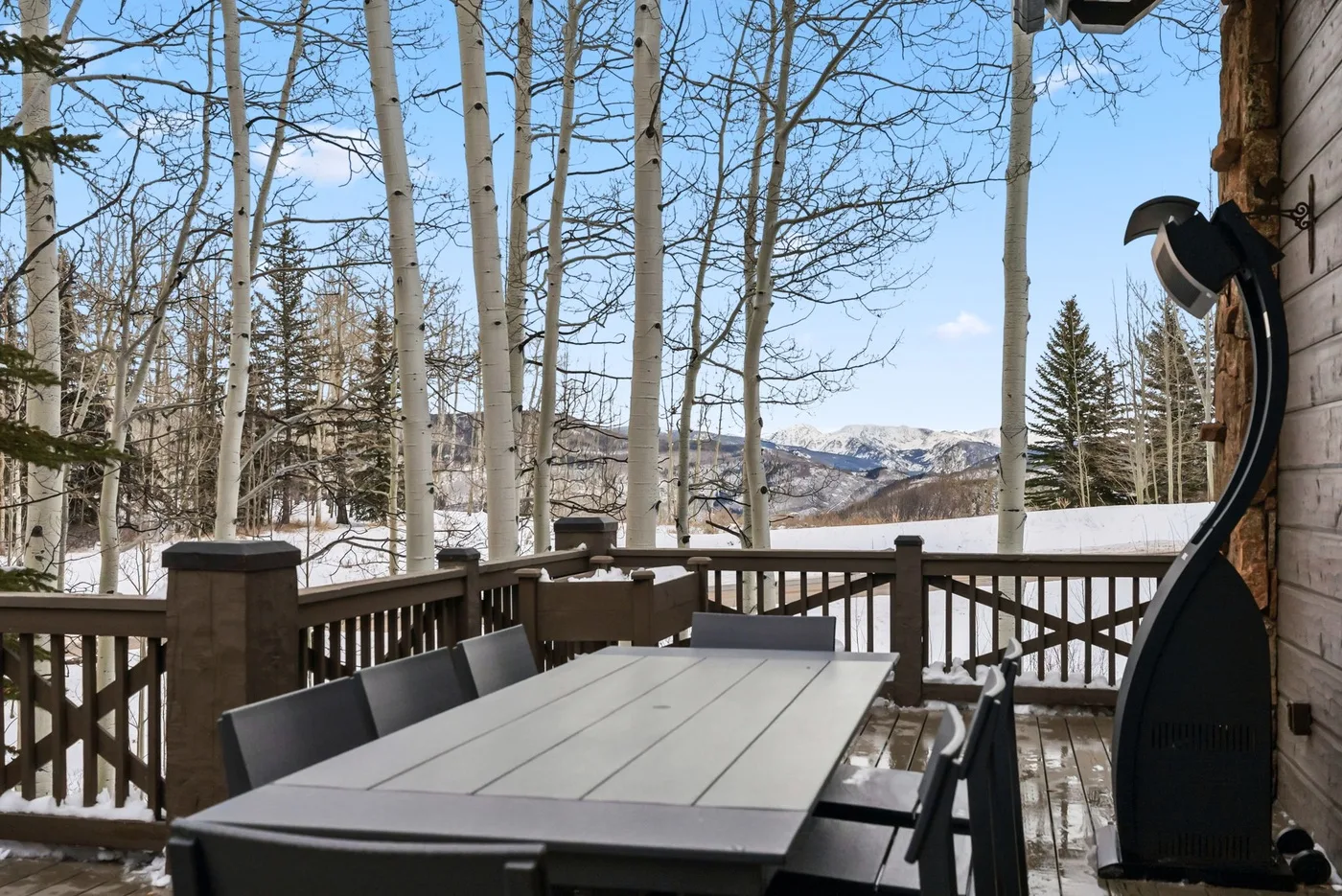 A deck with outdoor seating overlooks a snowy landscape and distant mountains.