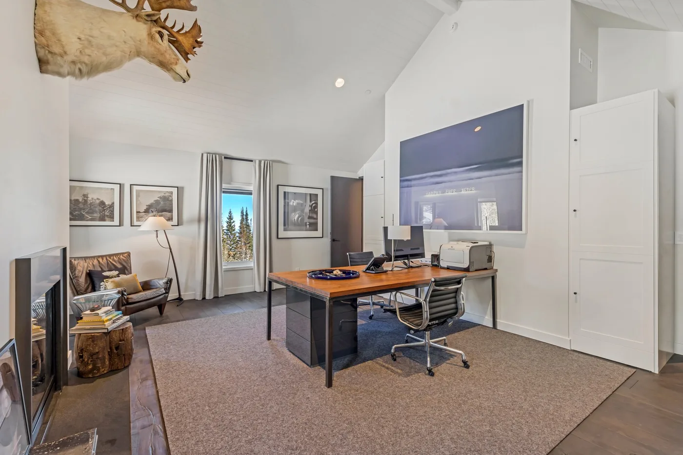 A bright attic office with a large desk, computer monitors, and a chair.