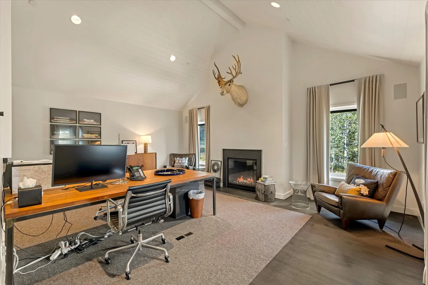 A bright living room and workspace with a desk, seating, and a fireplace.