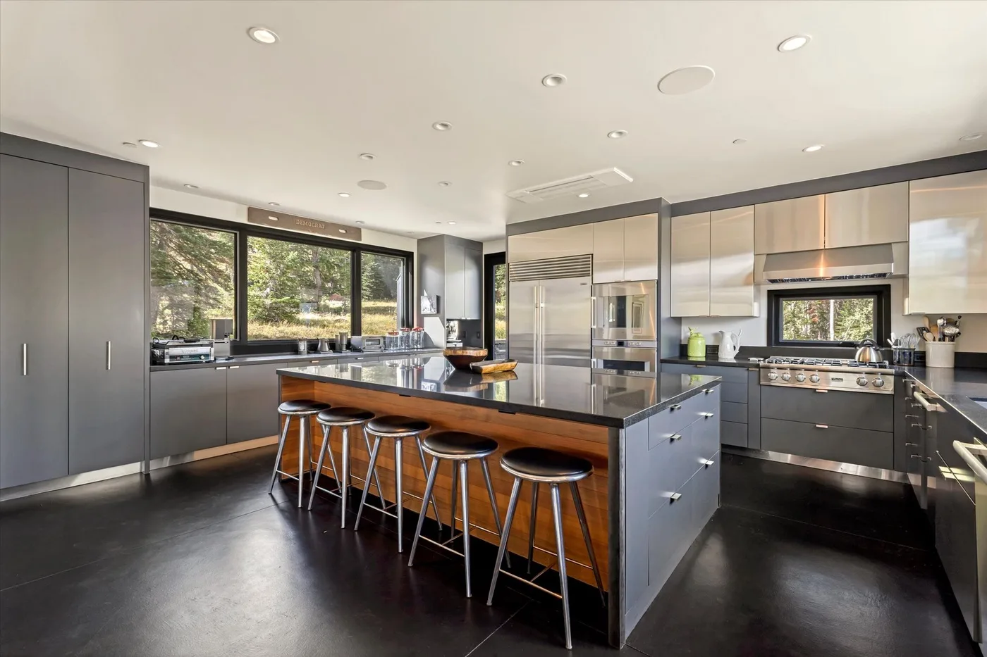 A modern kitchen with a central island and stools beneath large windows.